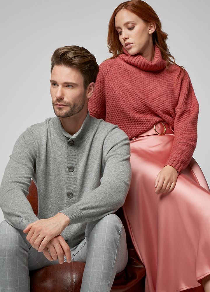 Un uomo in cardigan grigio e una donna in dolcevita rosa, seduti su una poltrona di pelle